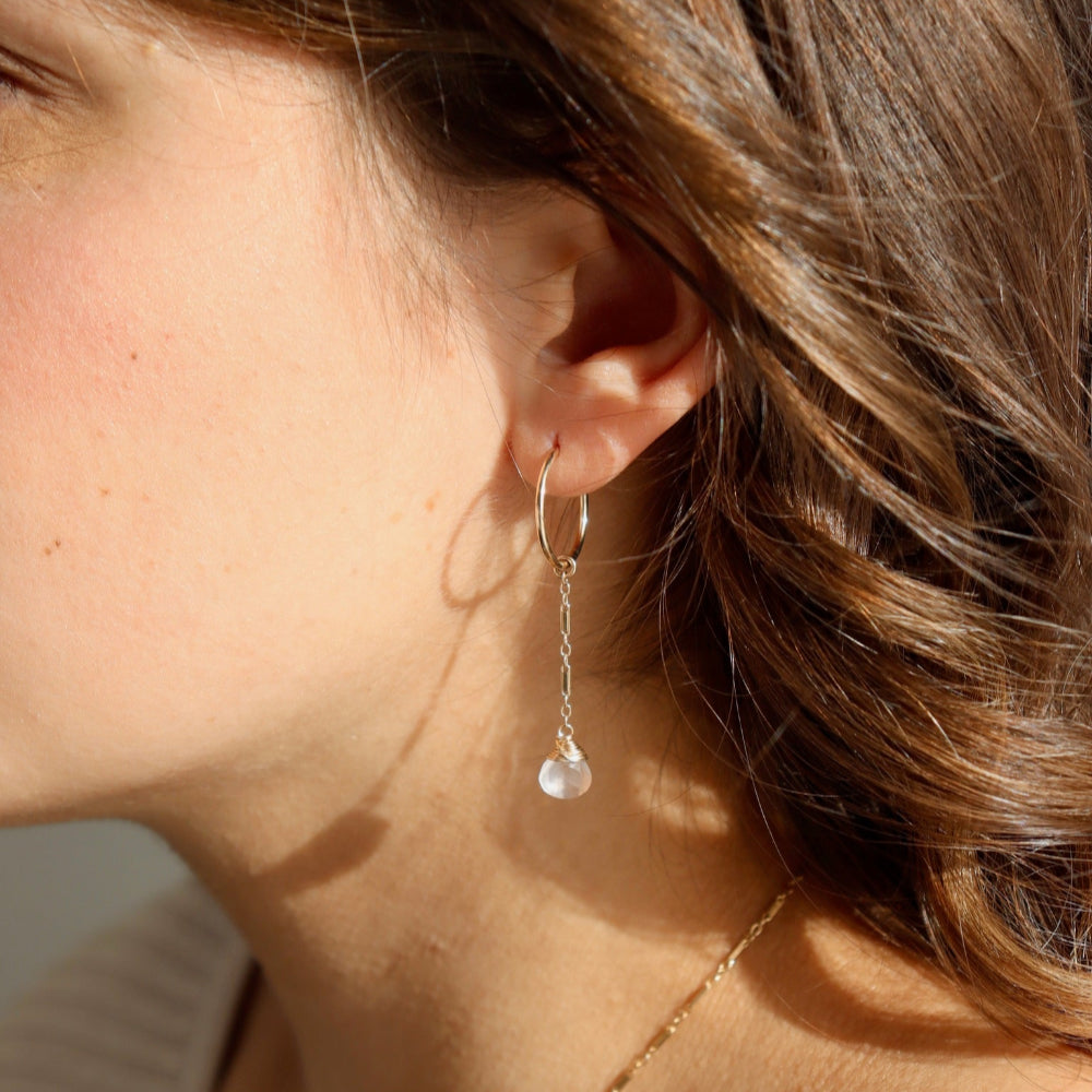 Model wearing the rose quartz marisol earrings. These earrings feature a 14k gold fill goldie hoops with our Marisol bar + link chain dropping down one inch. At the end of the chain is a wire-wrapped rose quartz gemstone