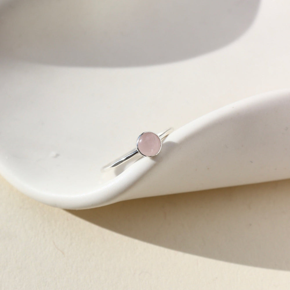 Sterling silver ring featuring a 5mm rose quartz gemstone set in a sterling silver thin band. The ring is displayed on a white dish. 