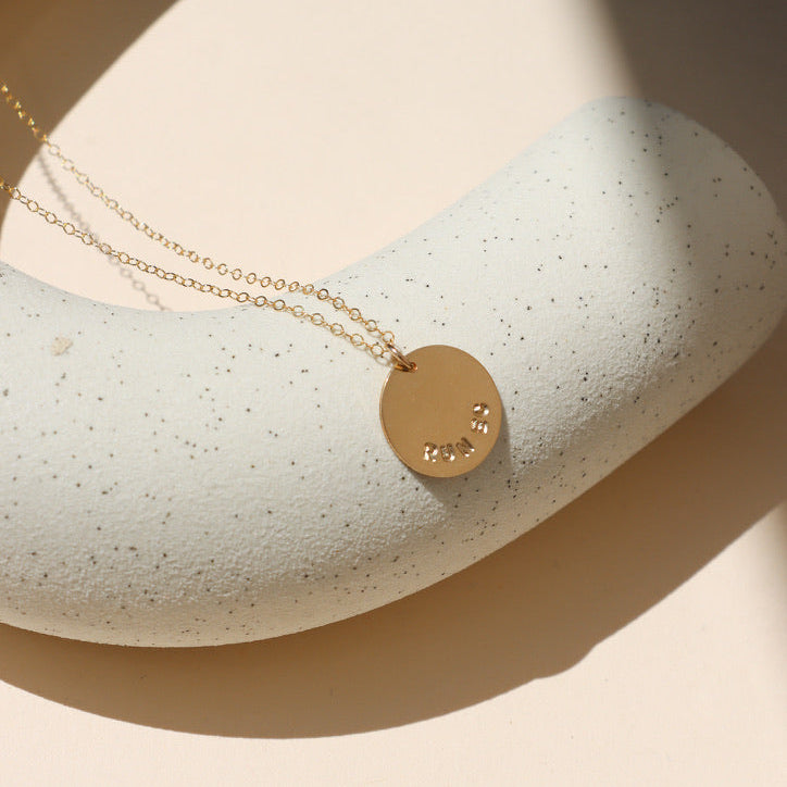 14k gold fill hand stamped round disc charm on a delicate chain necklace on a light surface