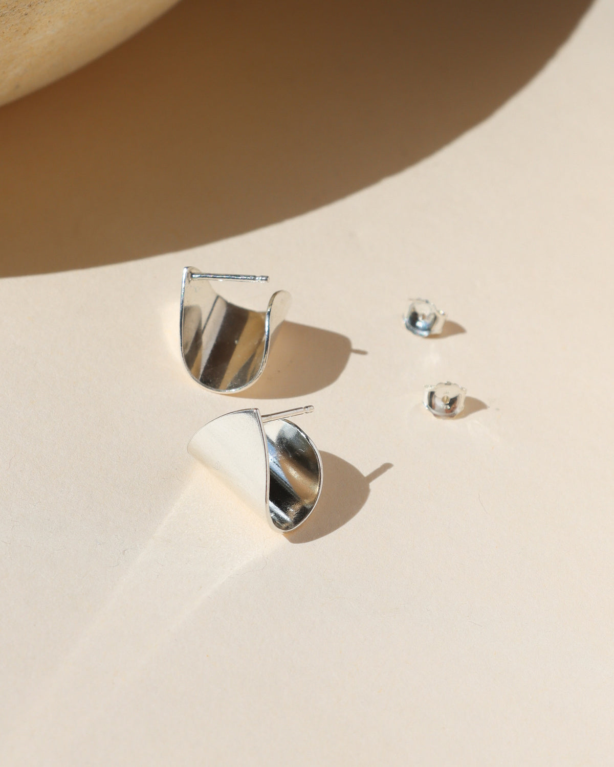 Sculptural sterling silver stud earrings with a polished folded design that catches and reflects the light.