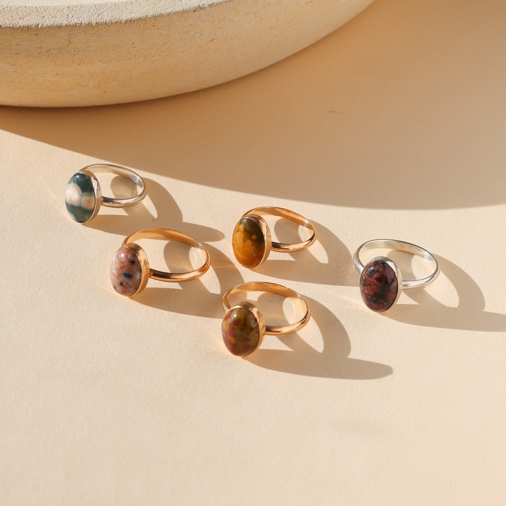 sterling silver and 14k gold fill rings with oval ocean jasper stones on a light surface