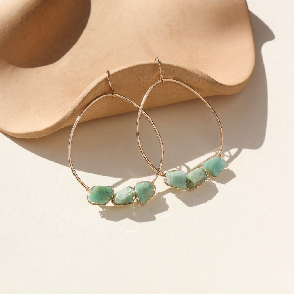 A 1.75 wide 14k gold fill wire hoop with three amazonite gemstones wire wrapped at the bottom of each earring. Earrings are displayed on a cream back drop. 