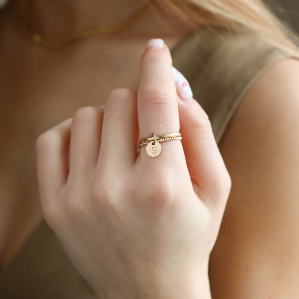Model wearing a smooth band stacked with a spiral 14k gold fill band, with a small "S" stamped disc attached to both rings. 