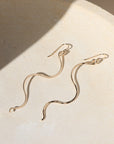 Gold snake-shaped earrings on a textured beige surface