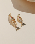 Large and small gold koi fish charms with red crystal eyes displayed on a neutral surface in warm natural light