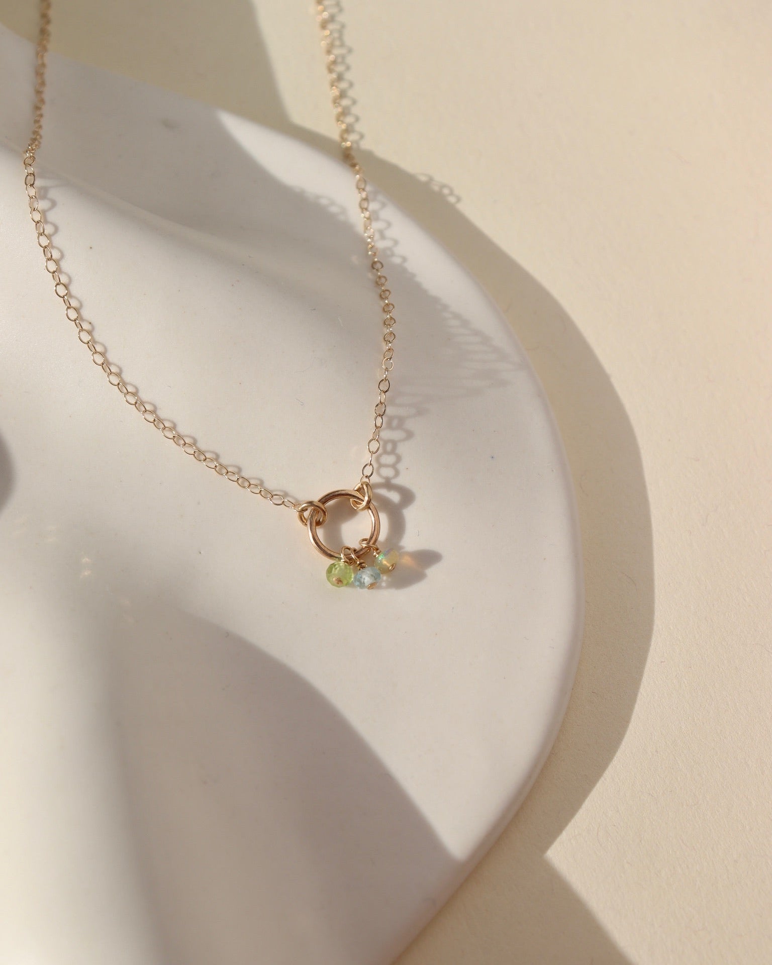lightly hammered 14k solid gold circle pendent with dainty chain and colorful birthstone beads laid in the sunlight