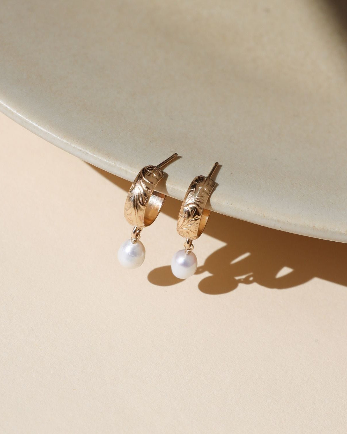 14k gold fill floral hoop studs with edison pearls dangling on a light dish