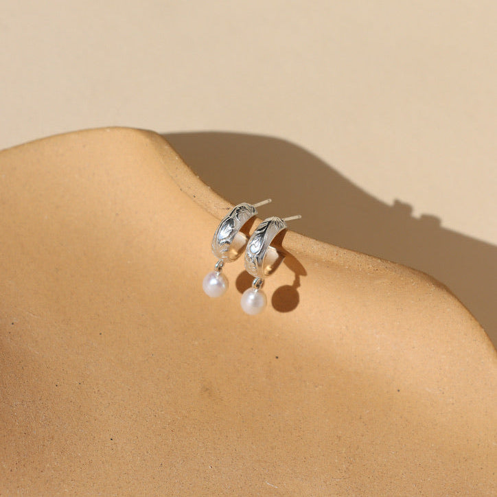 sterling silver textured hoop earrings with pearls dangling on a light dish
