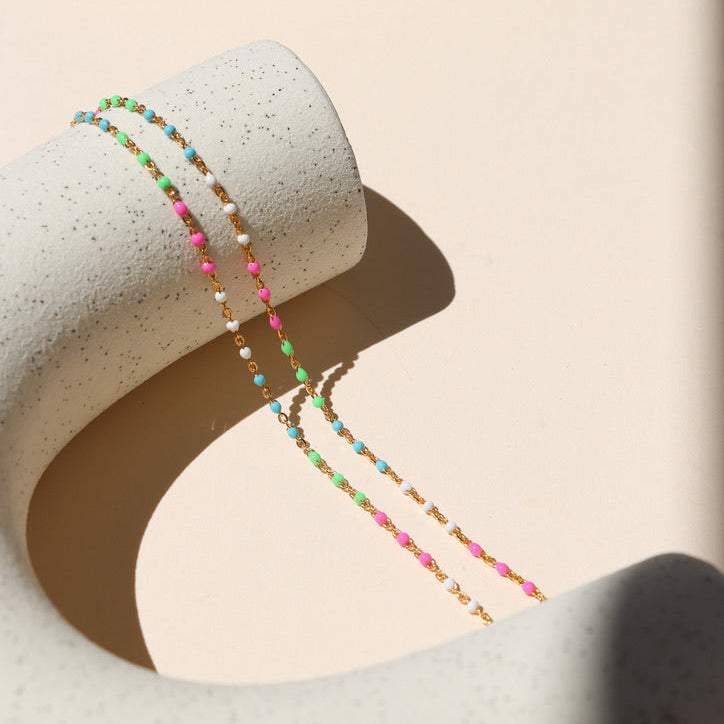 14k gold fill chain and multicolored enamel necklace on a light dish