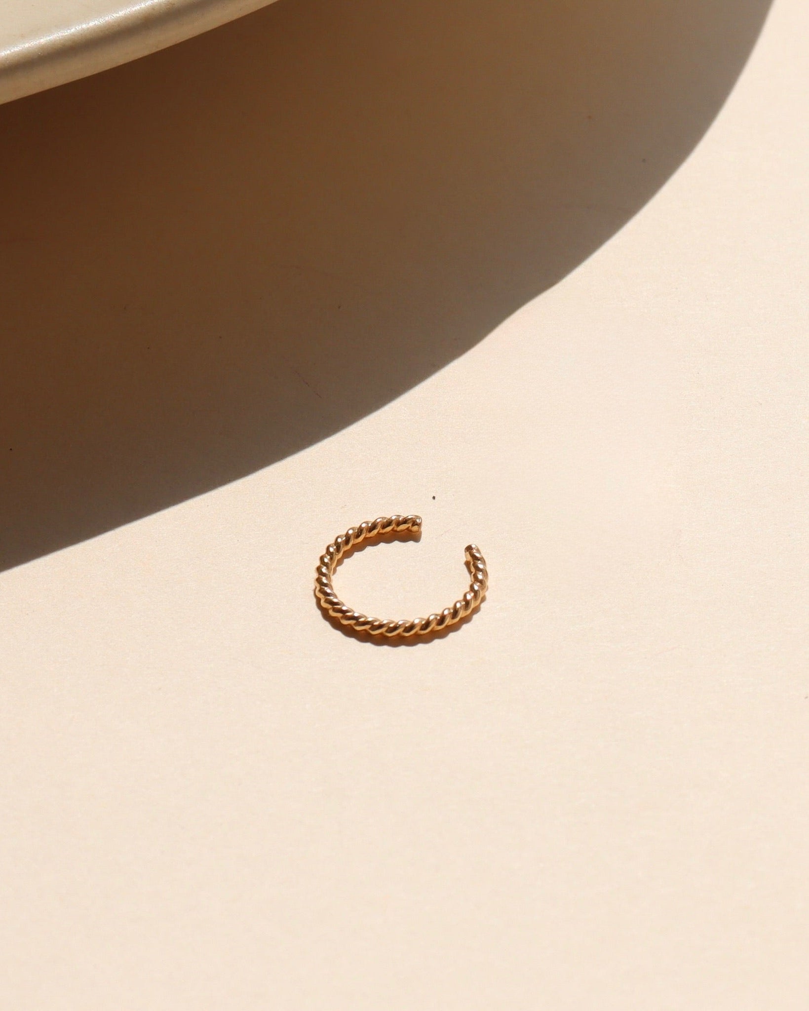 gold spiral ear cuff in the sunlight on a light dish