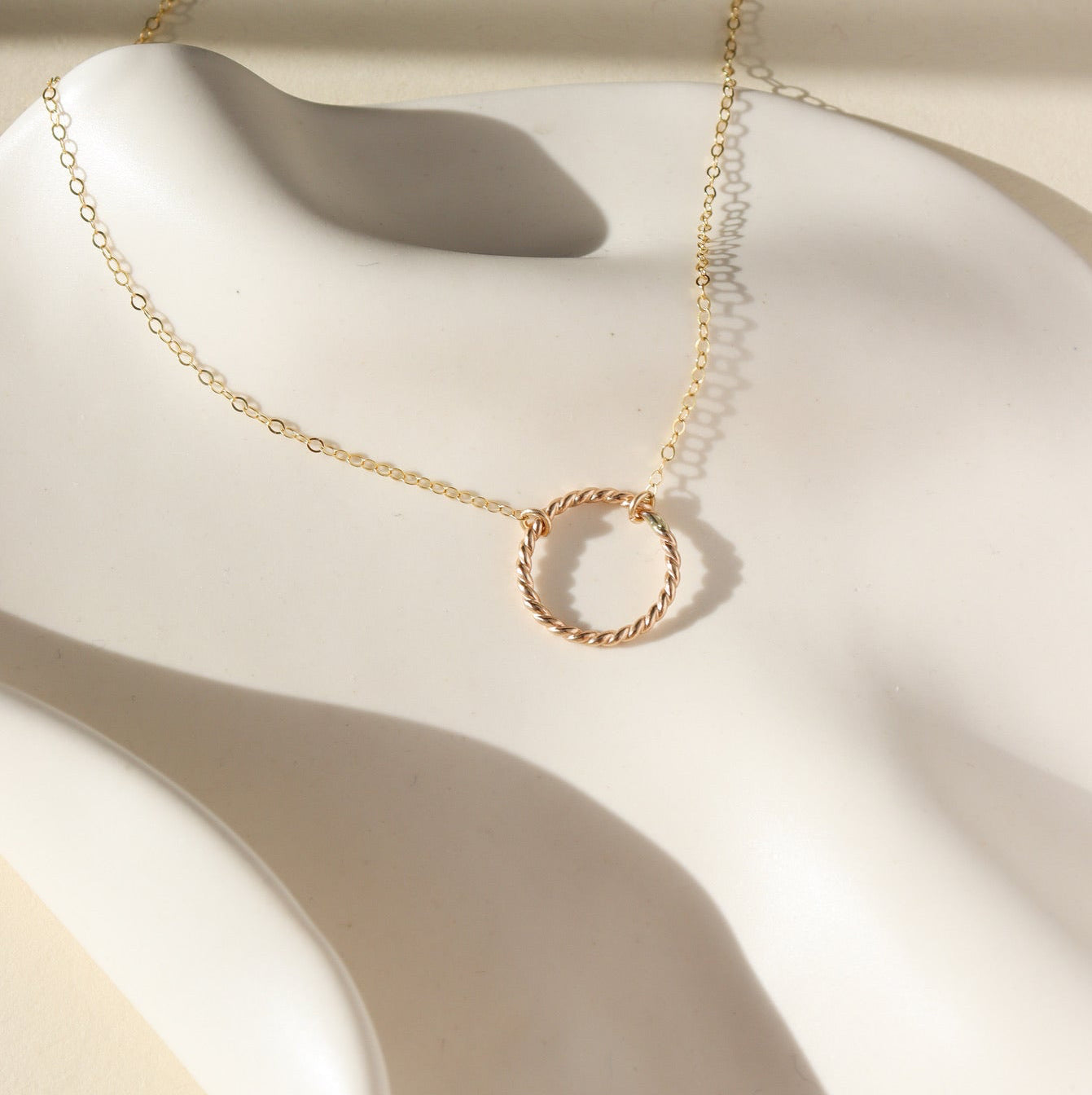 14k gold fill spiral circle pendant on a dainty chain displayed on a white plate