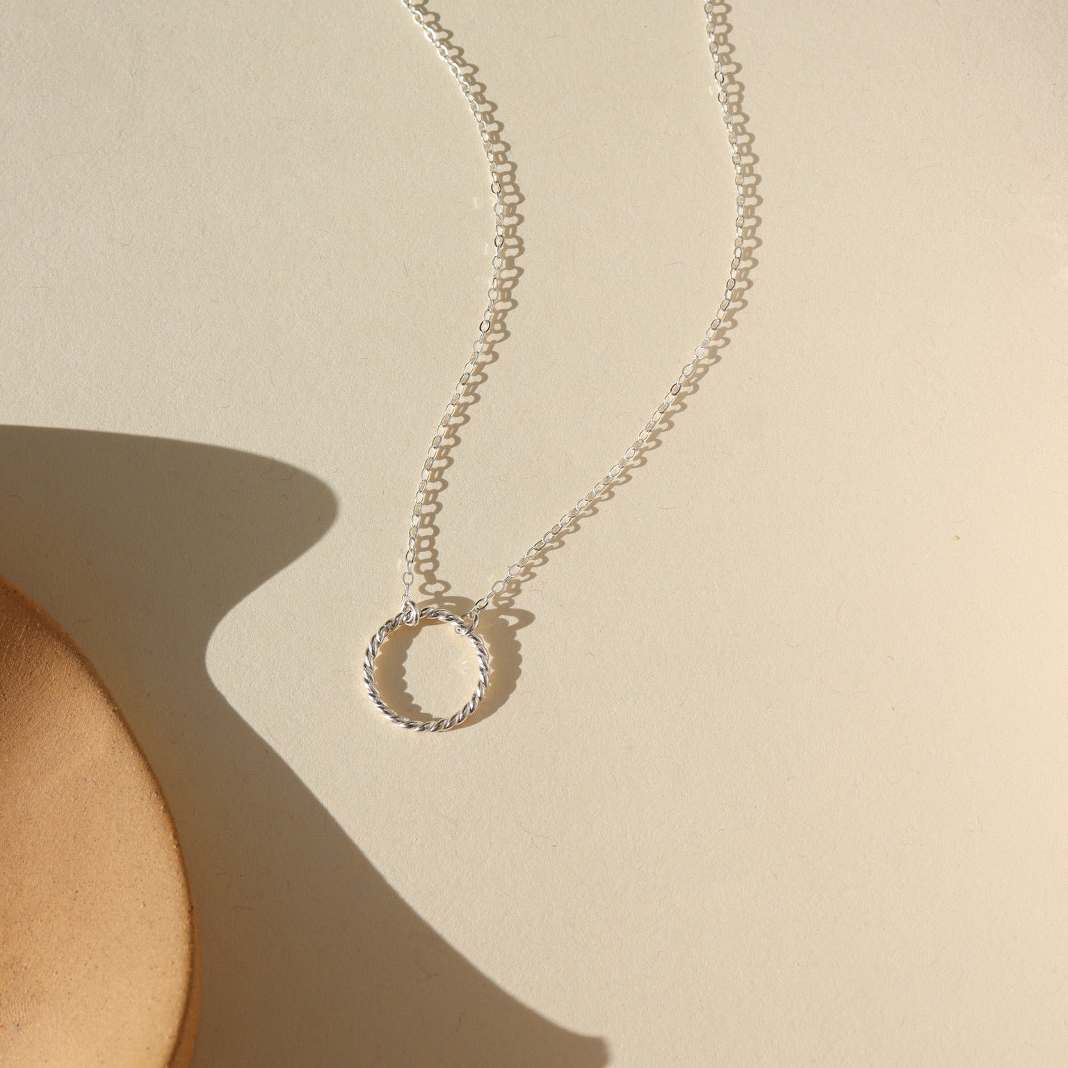 sterling silver spiral circle pendant on a dainty sterling silver chain in the sunlight