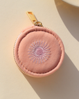 Pink round jewelry case with gold zipper on a beige background