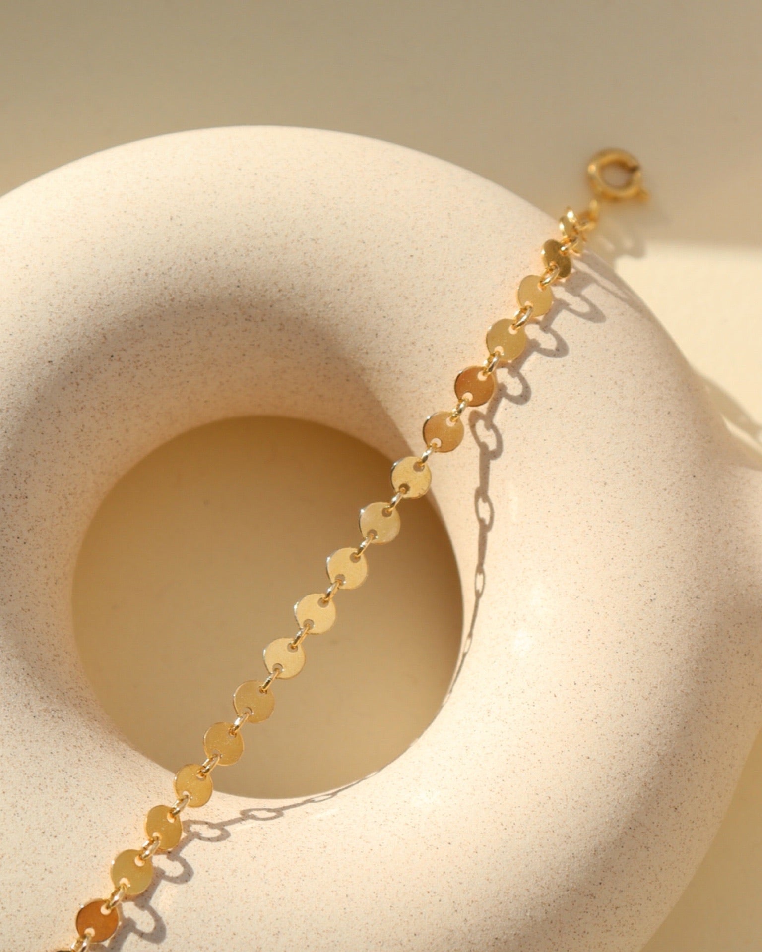 Starlight Bracelet featuring polished disc chain links styled on a textured ceramic form in natural light.