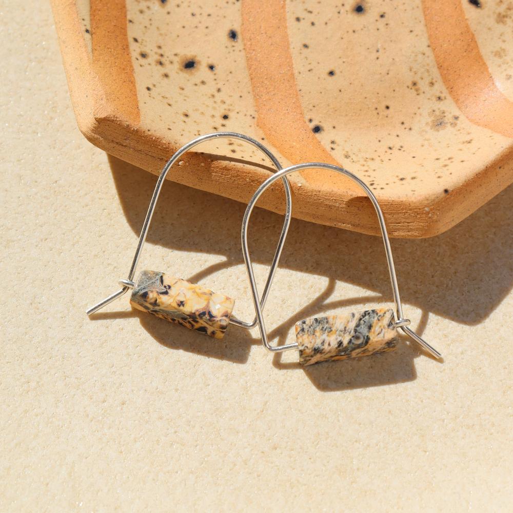 Sterling Silver Leopard Skin Jasper Arch Earrings by Token Jewelry laying next to a speckled ceramic plate