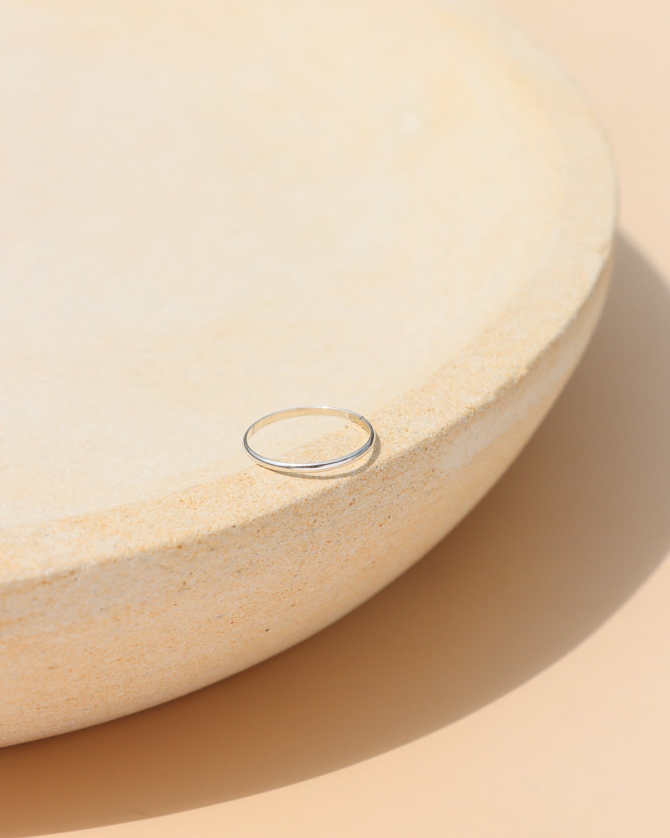 Sterling silver minimalist stacking ring with a thin polished band, modern everyday jewelry displayed on a ceramic jewelry tray in natural sunlight.