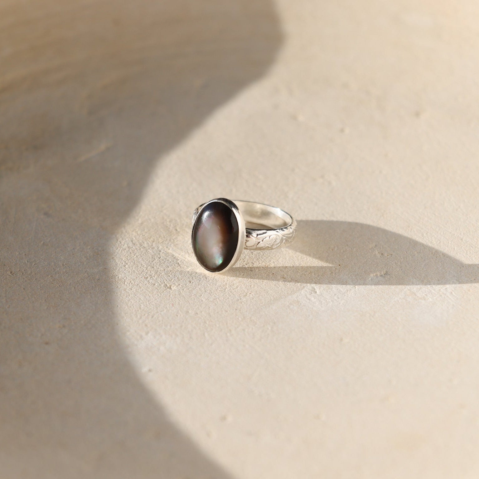Moonflower rings in gold and silver with oval luminous stones, styled on a neutral surface in soft natural light.