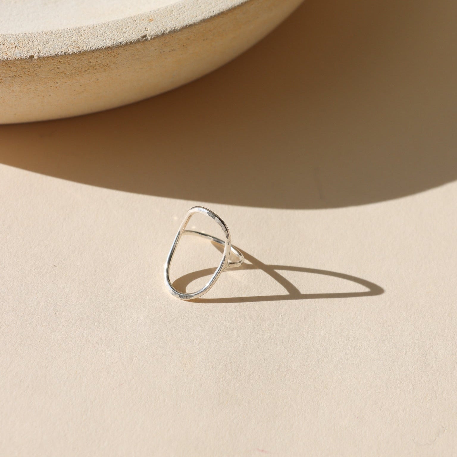 Sterling silver geometric open ring with an organic freeform shape, photographed on a neutral surface in soft natural light.
