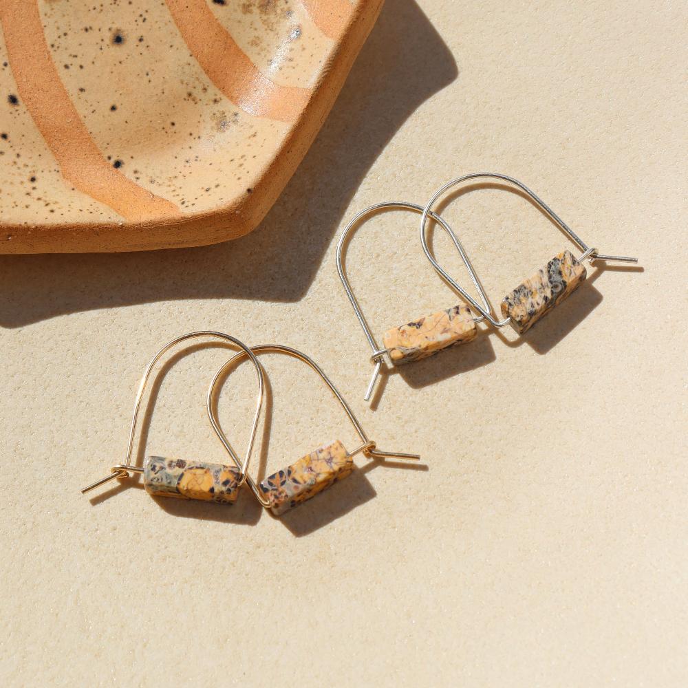Sterling Silver and 14k gold fill Leopard Skin Jasper Arch Earrings by Token Jewelry laying next to a speckled ceramic plate