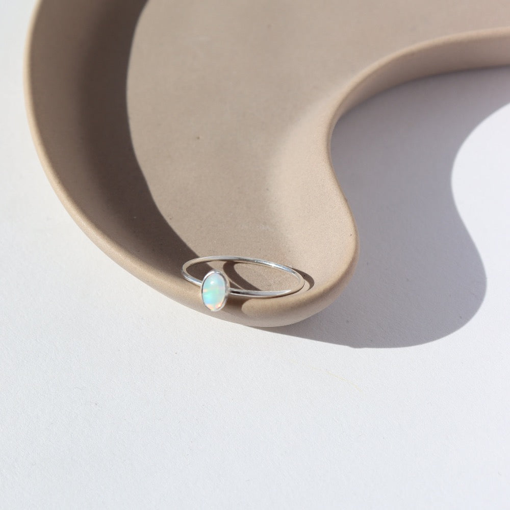 925 sterling silver Opal Essence Ring laid on a white plate in the sunlight. This ring features a smooth band with oval opal. These pair great with our stacking rings.