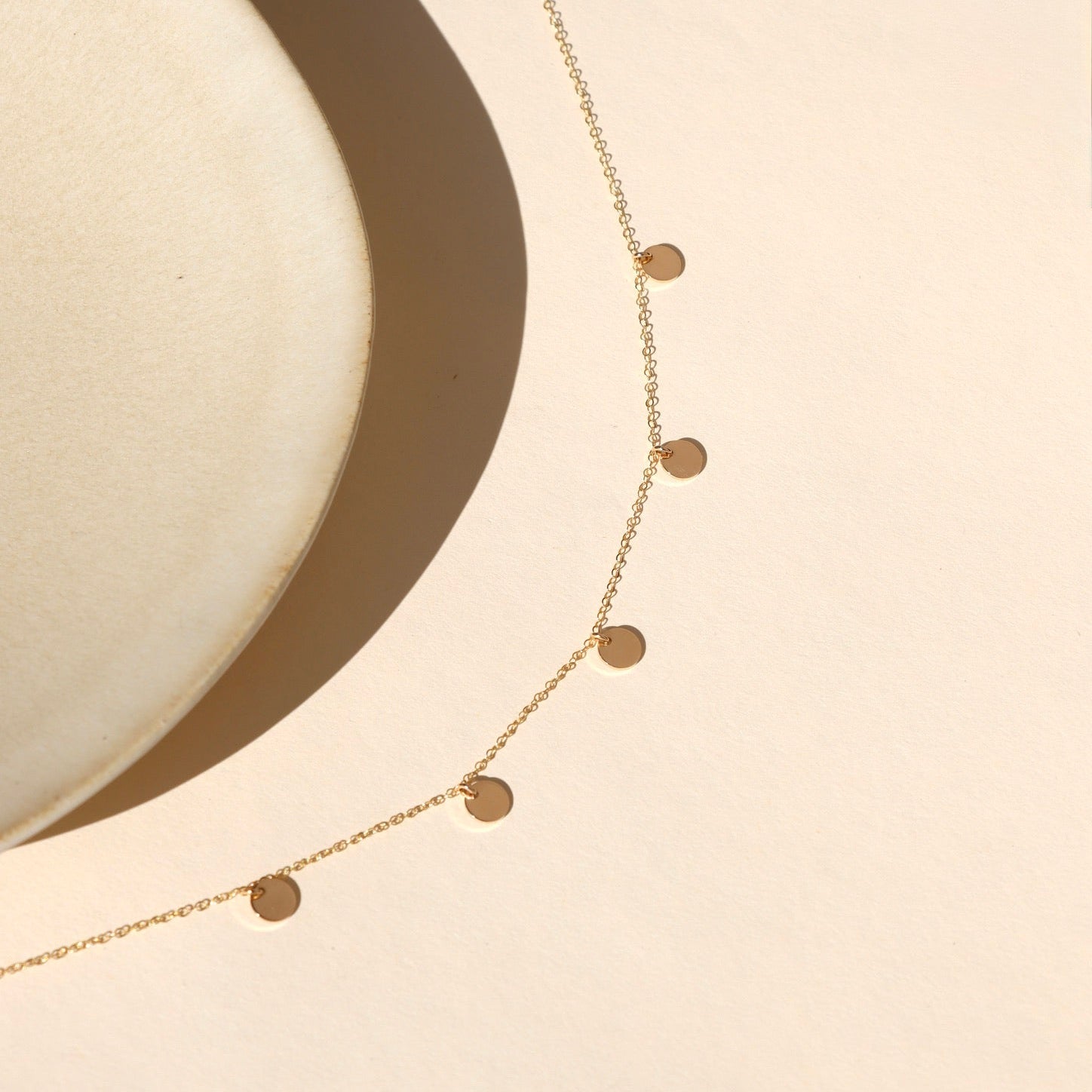 14k gold fill delicate chain necklace with 5 small gold discs on a light surface