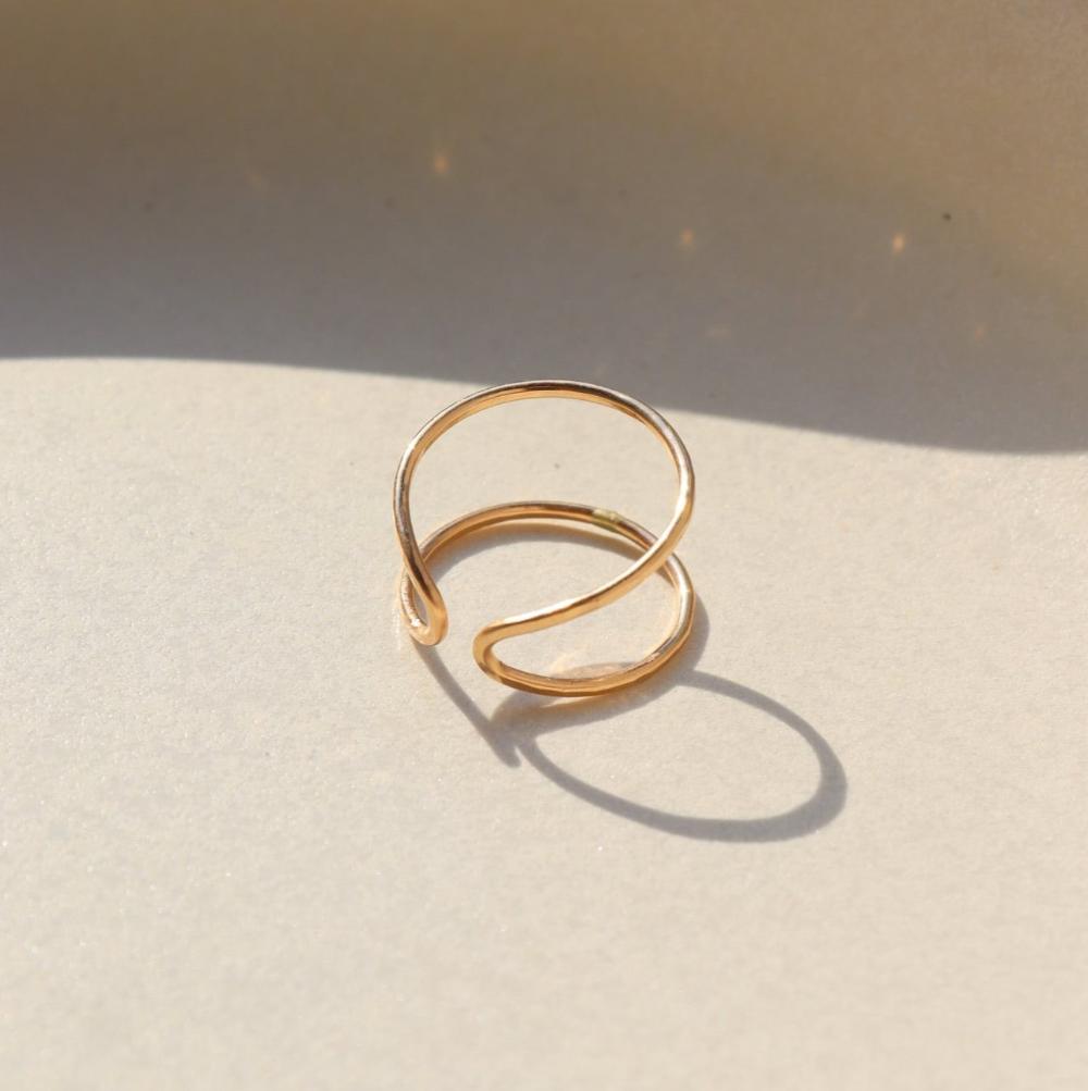 14k gold fill hammered and hand shaped ring laid on a tan plate in the sunlight