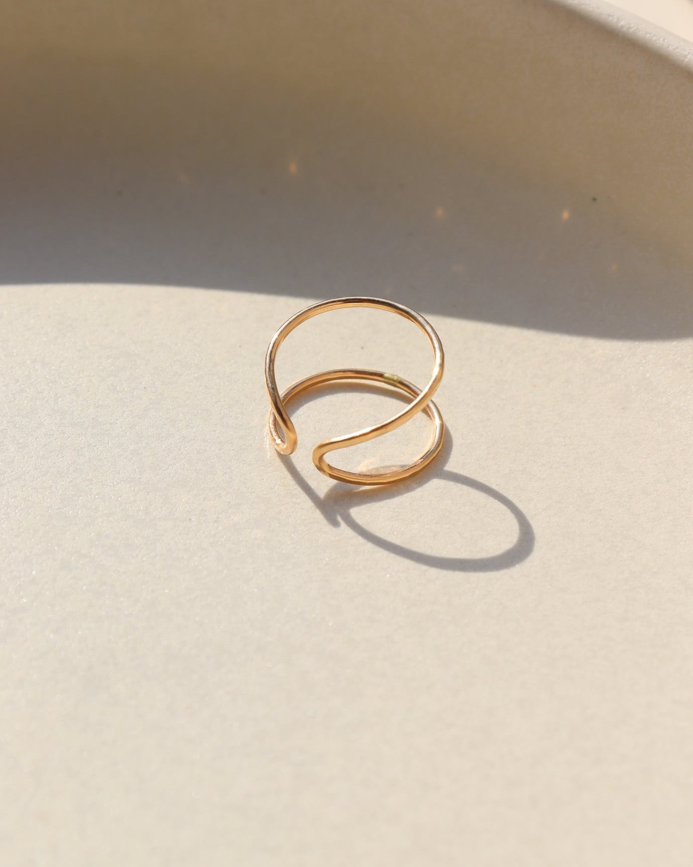 14k gold fill hammered and hand shaped ring laid on a tan plate in the sunlight