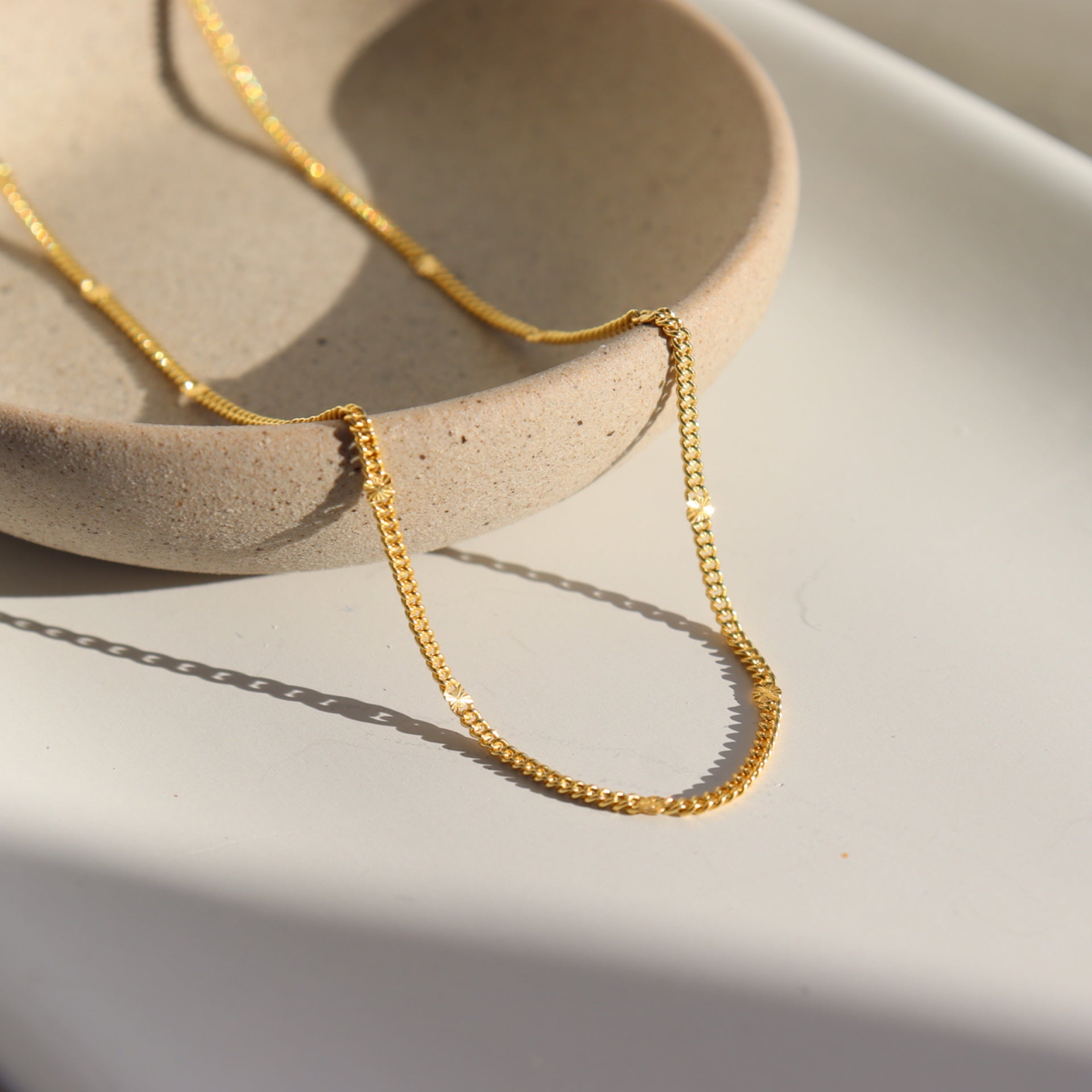 14k gold fill Sunny Chain laid in the sunlight on a tan plate. This necklace features a simple chain with an extra sparkle every 1/2&quot;