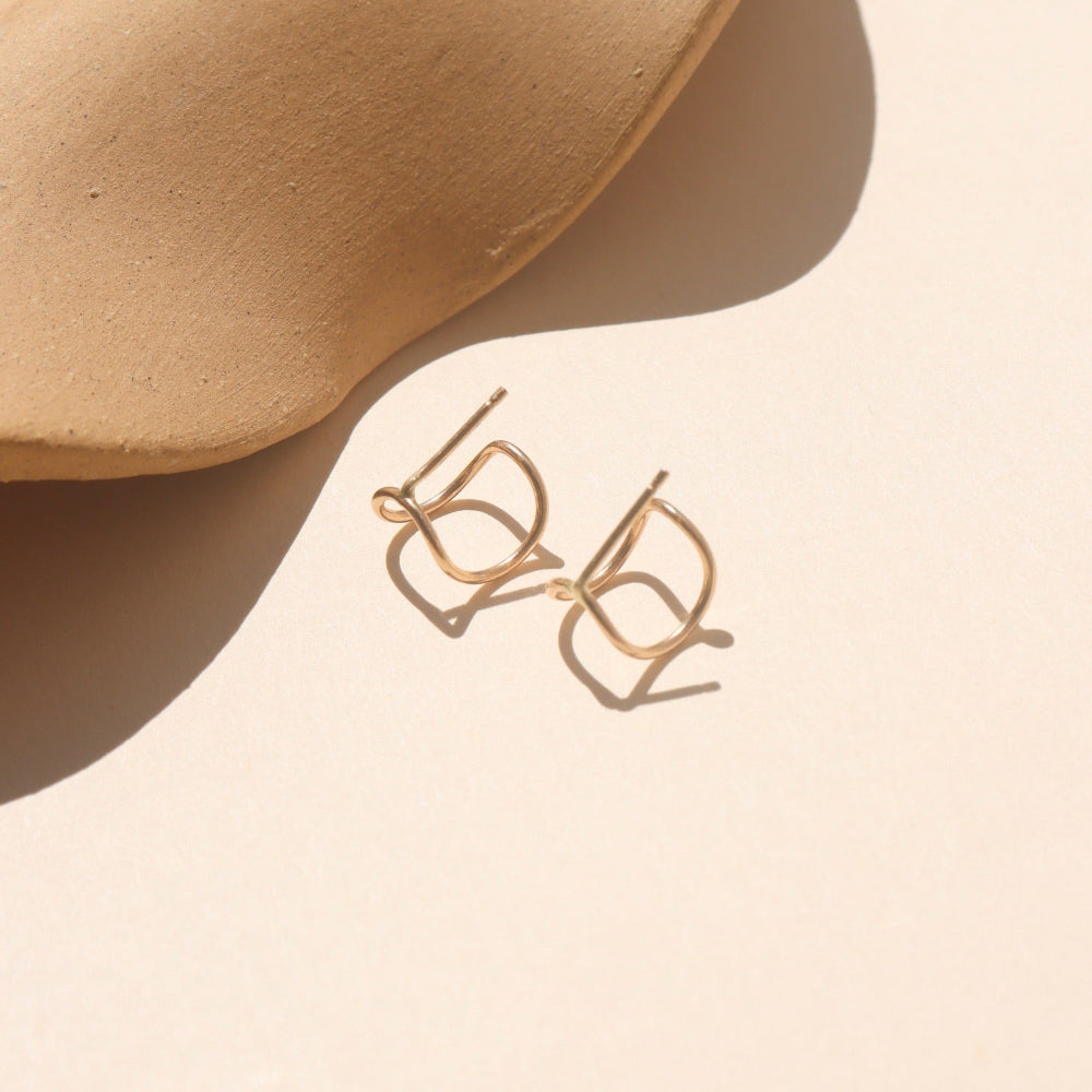 Curved 14k gold fill wire stud designed to wrap around the ear, displayed on a cream backdrop in natural sunlight