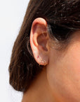 Model wearing a curved 14k gold fill wire stud designed to wrap around the ear, model paired it with a pink tourmaline stud set in 14k gold fill 