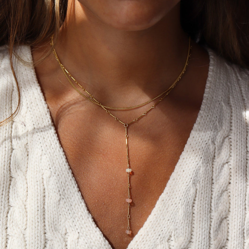 Model wearing a 14k gold fill bar and link chain with three peach opal gemstones. 
