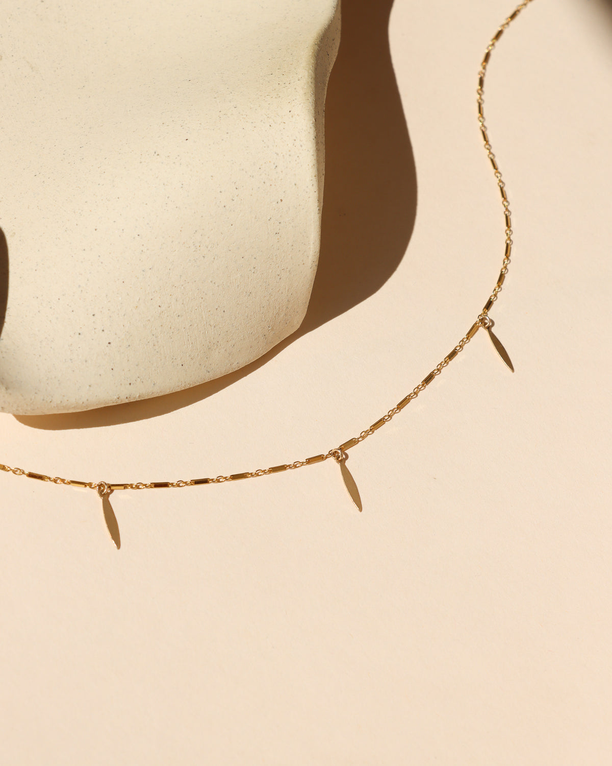 Delicate gold chain necklace with three elongated leaf-shaped dangle charms.