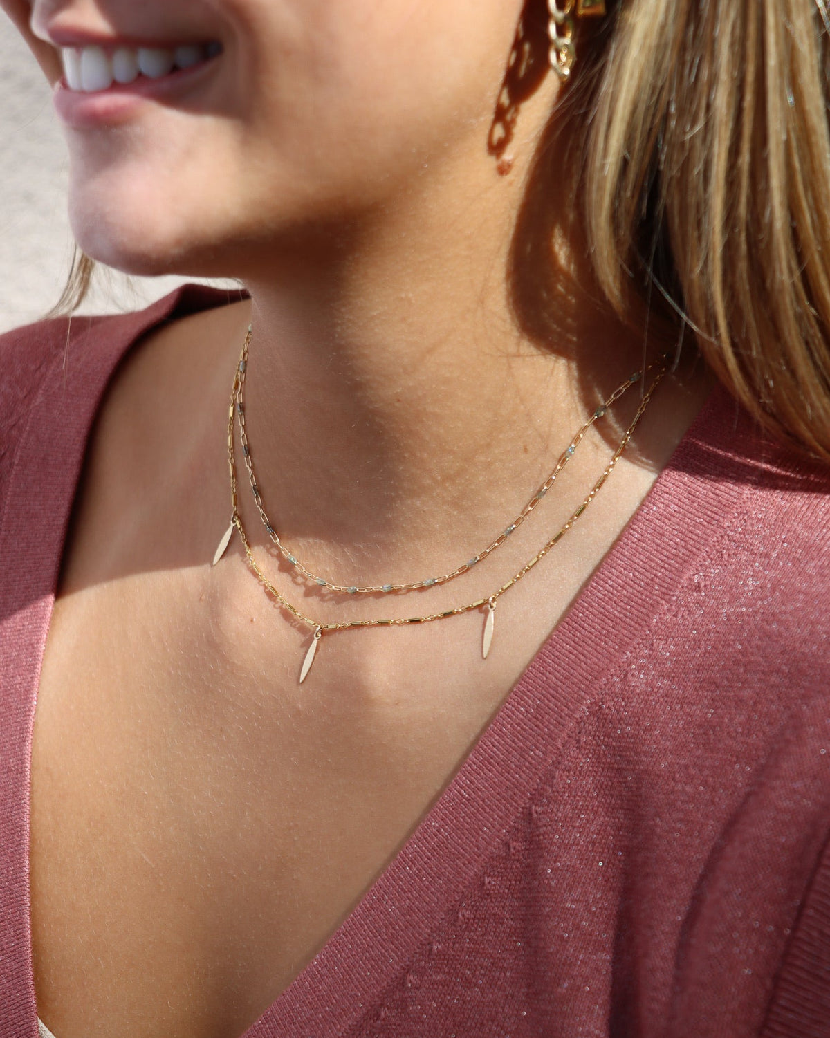 Gold charm necklace with three elongated leaf-shaped dangles, layered with a delicate mixed-metal link chain.