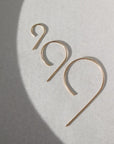 14k gold fill nine earrings laid on a gray plate in the sunlight. These earring give the effect of the number 9.