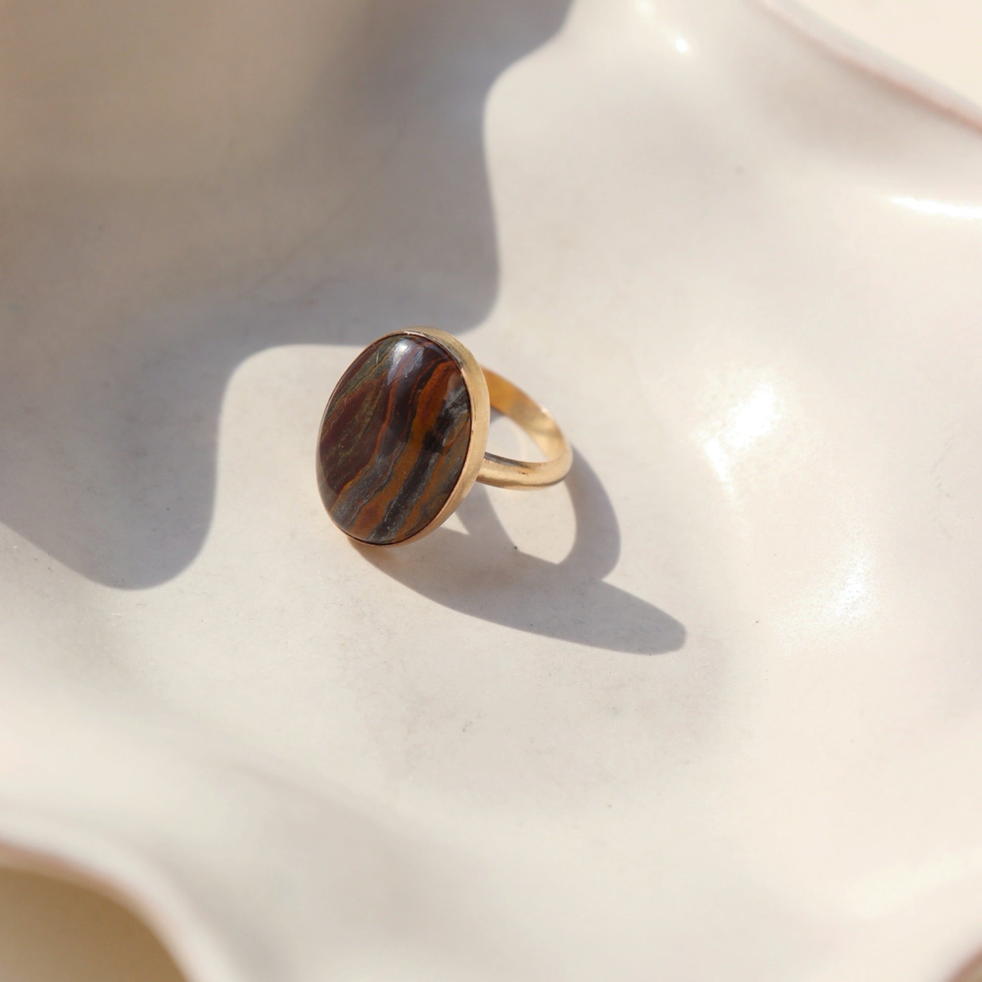 The Woodland Ring by Token Jewelry features a large striped Tiger Eye gemstone on a simple 14k gold fill band, photographed on a white dish