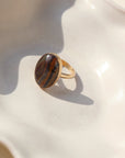 The Woodland Ring by Token Jewelry features a large striped Tiger Eye gemstone on a simple 14k gold fill band, photographed on a white dish