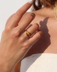 An amber-colored Tiger Eye gemstone on a horizontal bezel on a 14k gold fill band, photographed on a model