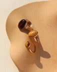 An amber-colored Tiger Eye gemstone on a horizontal bezel on a 14k gold fill band, photographed next to two other rings with larger mookite gemstones