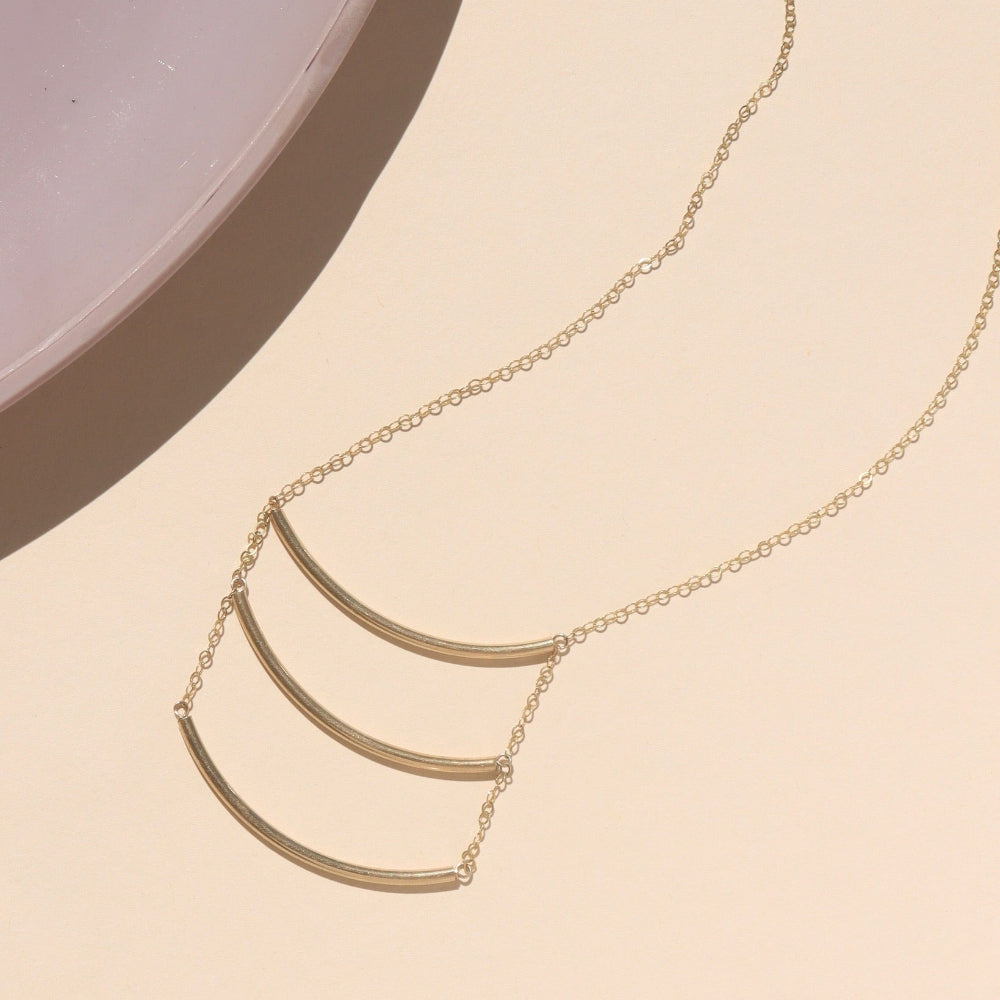 14k gold fill pendant necklace with three curved metal bars, displayed in natural sunlight