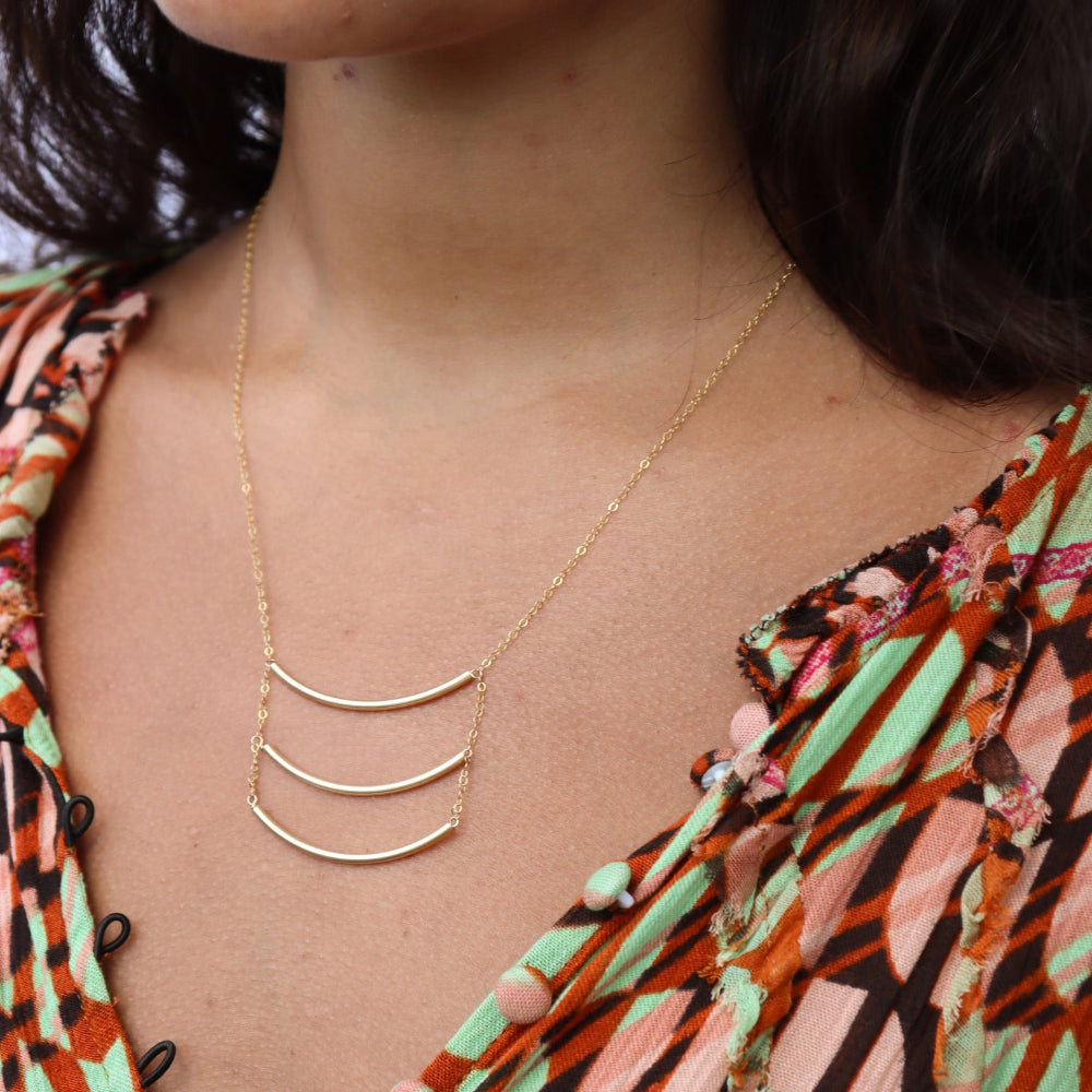 Model wearing a 14k gold fill pendant necklace with three curved metal bars
