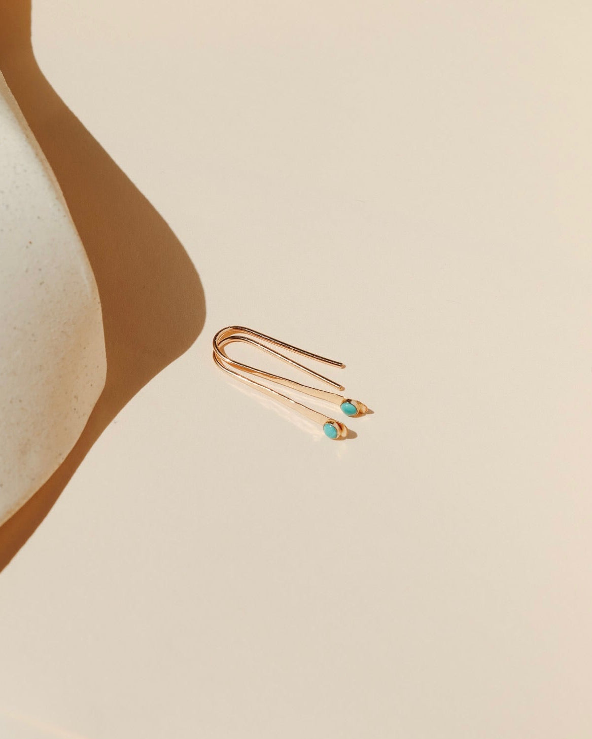 14k gold fill arc shaped earrings with small turquoise stones in the sunlight