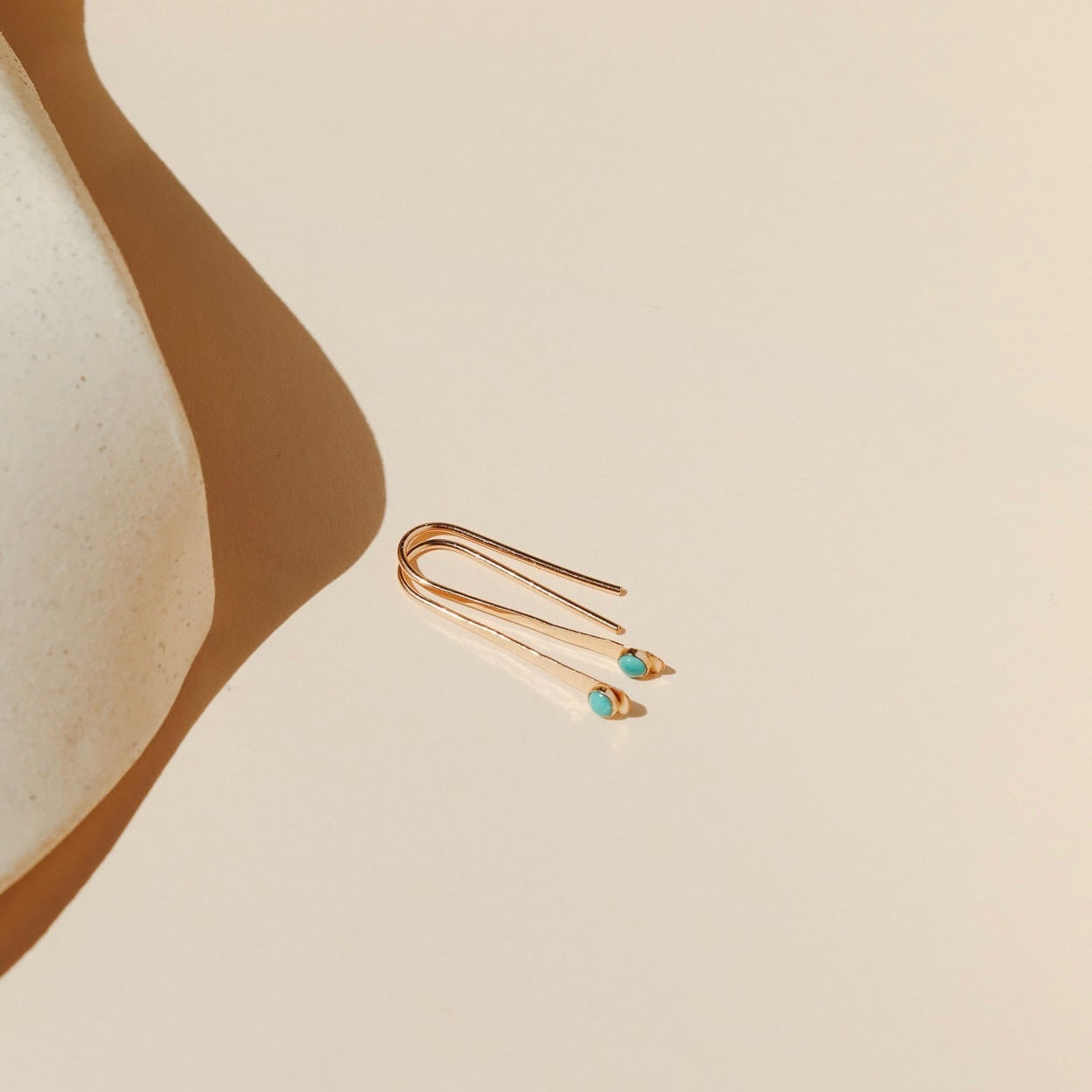 14k gold fill arc shaped earrings with small turquoise stones in the sunlight