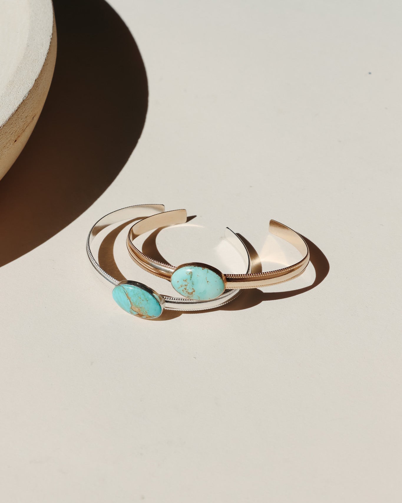 14k Gold Fill and Sterling Silver bezel set turquoise cuff on a smooth thick band with textured edges photographed on a beige background in the sunlight