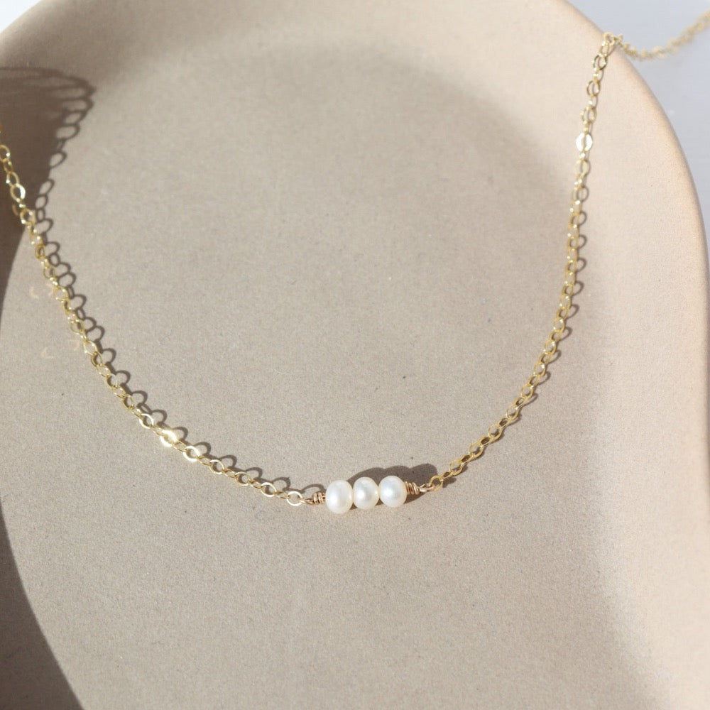 three freshwater pearls lined up on a 14k gold fill simple chain, made by Token Jewelry , photographed on a white ceramic dish