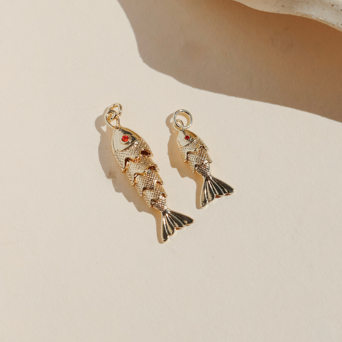 Large and small gold koi fish charms with red crystal eyes displayed on a neutral surface in warm natural light.