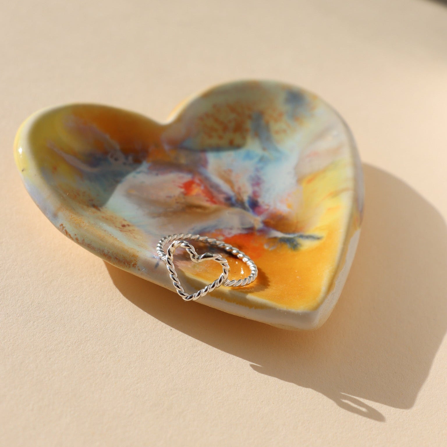 sterling silver spiral heart shaped ring displayed on multicolored heart dish