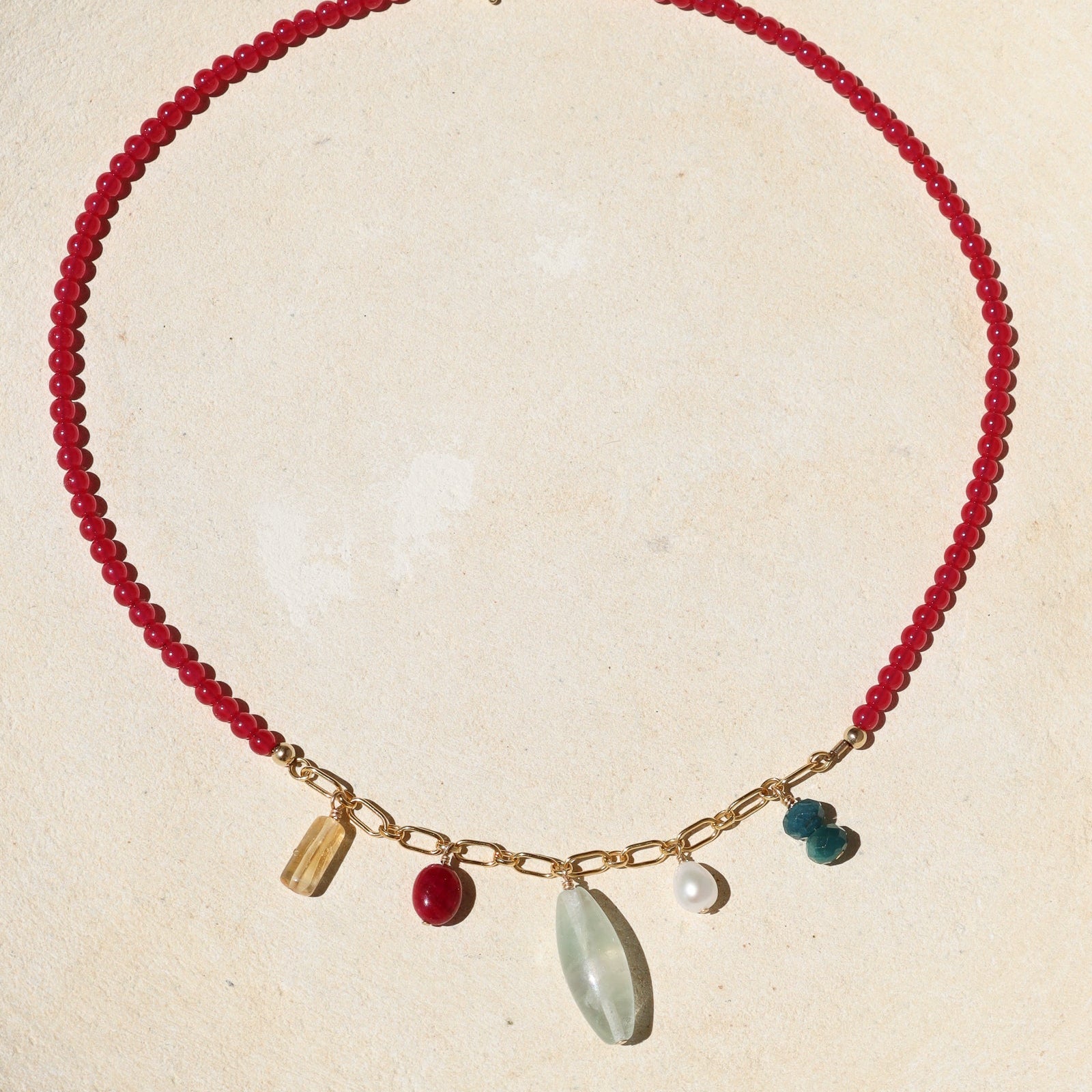 necklace with ruby beads and gold chain with gemstone charms on a light dish