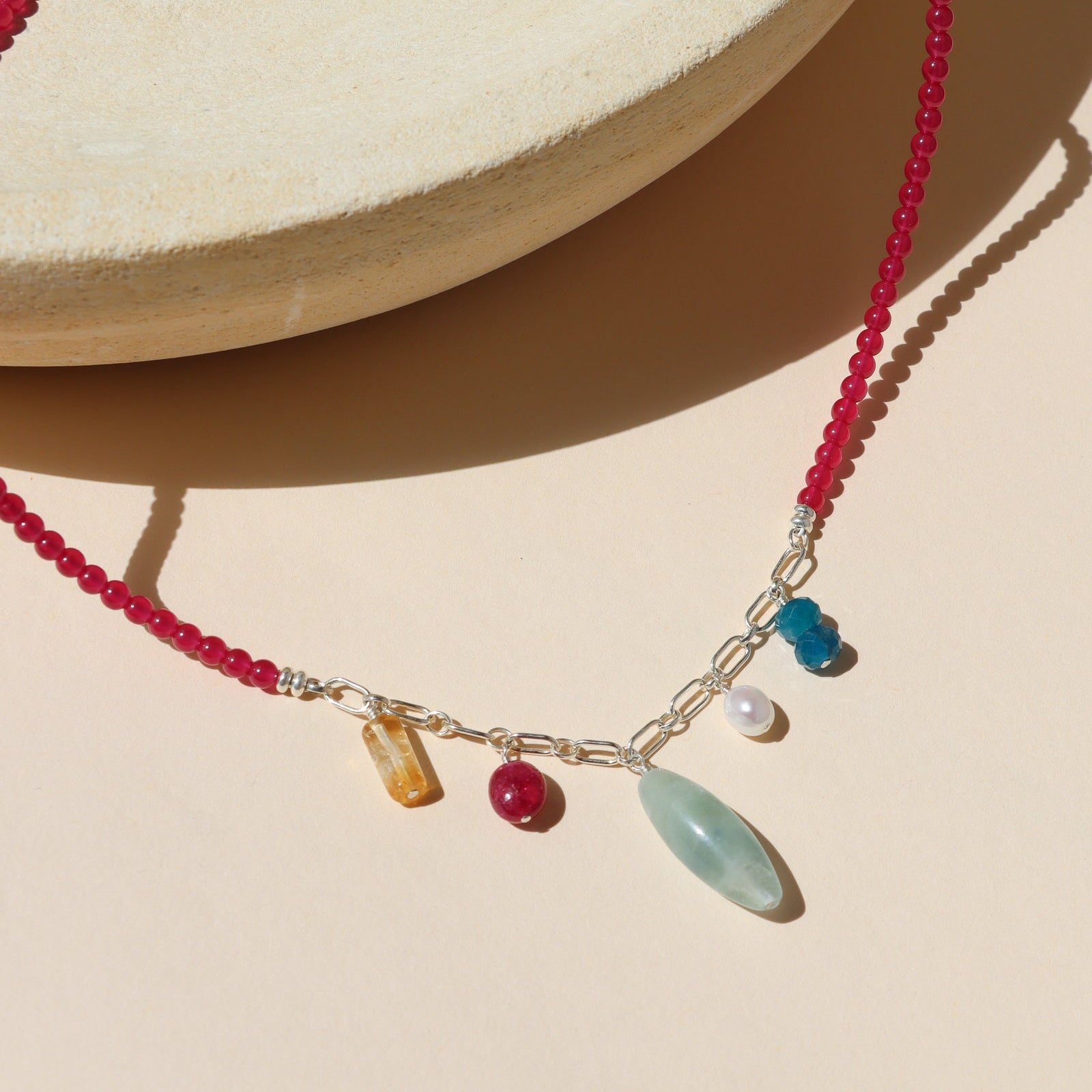 necklace with ruby beads and silver chain with gemstone charms on a light dish