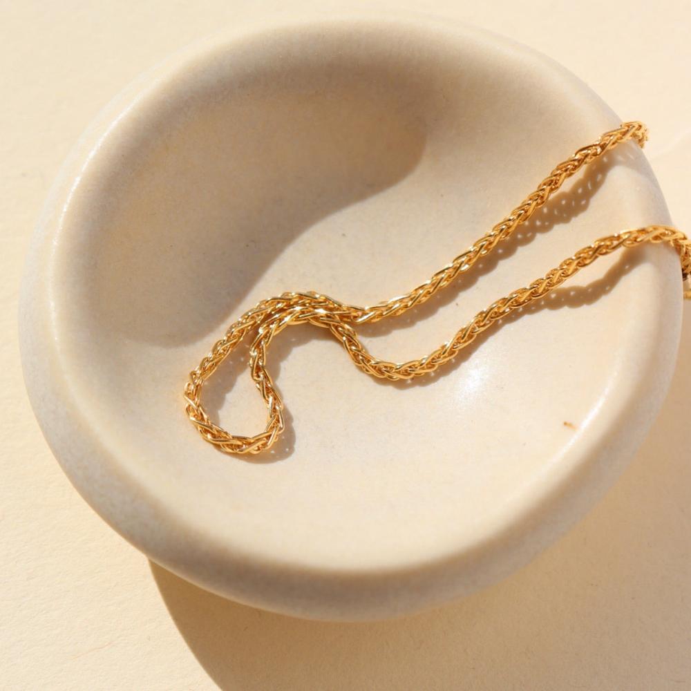 Westly bracelet by Token Jewelry photographed on a dish. The bracelet is a delicate 14k gold wheat-inspired chain.