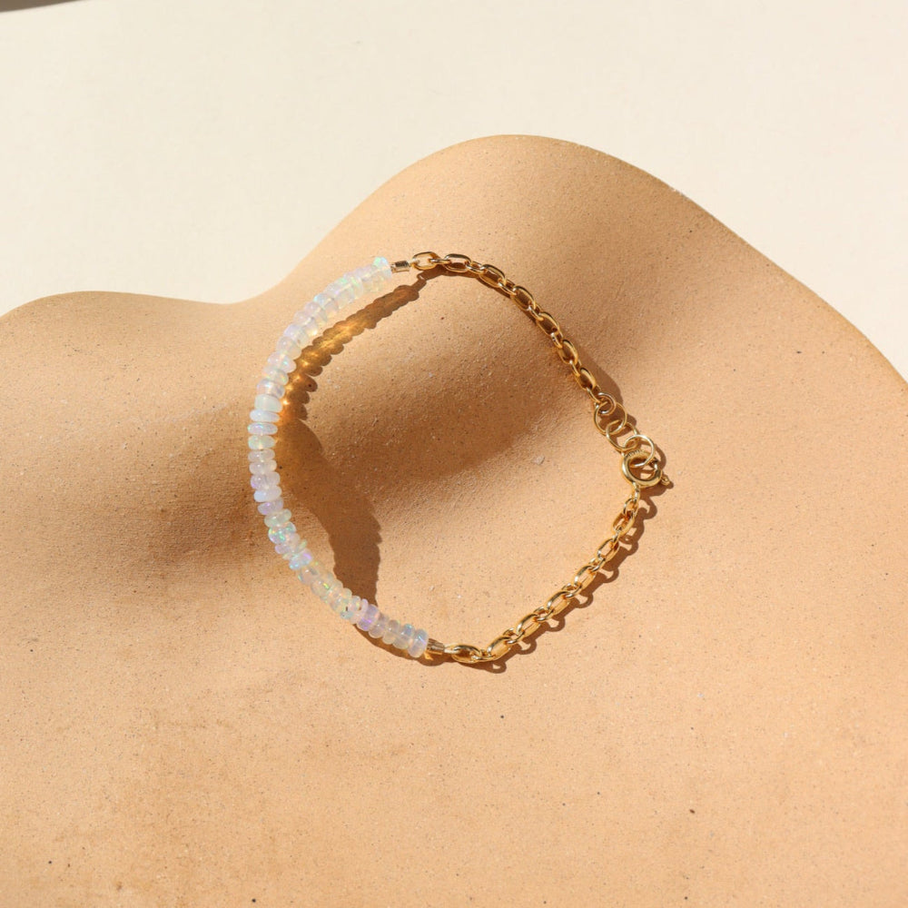 A 14k gold fill half and half bracelet featuring white opal gemstones and a rolo chain with a standard gold clasp. The bracelet is displayed on a orange backdrop in the sunlight. 